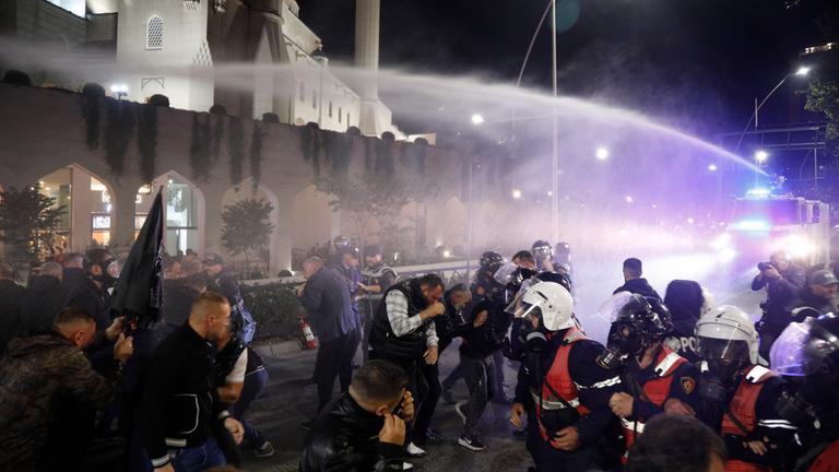 Demonstrierende auf den Straßen von Tirana. Die Polizei spritzt mit einem Wasserwerfer auf die Menschen.