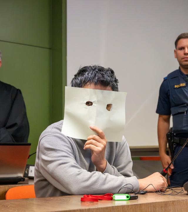 Bayern, München: Der Angeklagte sitzt zum Prozessauftakt auf seinem Platz im Gerichtssaal des Landgerichts München und verdeckt sein Gesicht. 