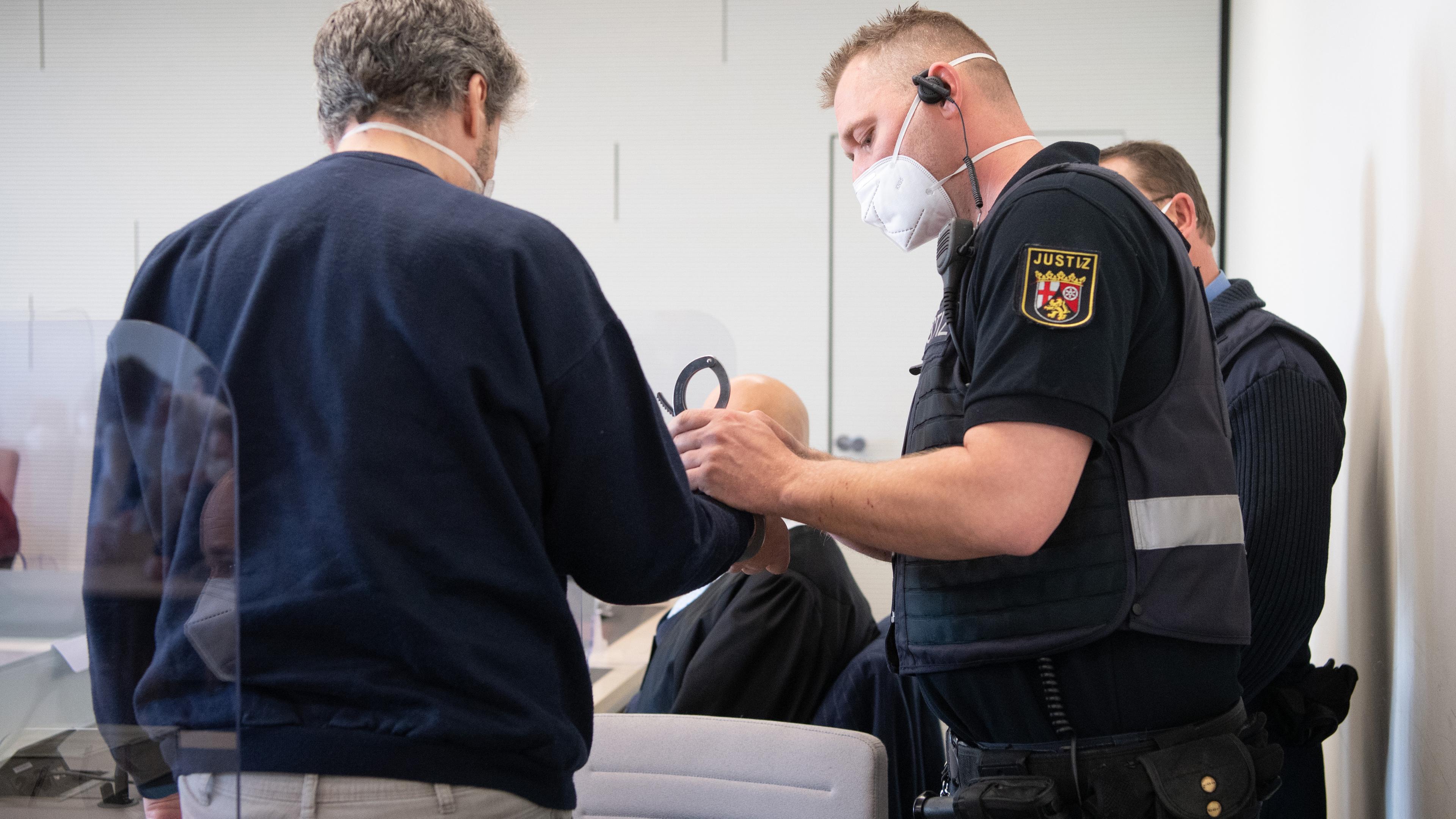 Rheinland-Pfalz, Bad Kreuznach: Der Angeklagte wird in Handschellen in den Gerichtssaal gebracht. Ein Justizwachtmeister nimmt ihm die Handschellen ab.