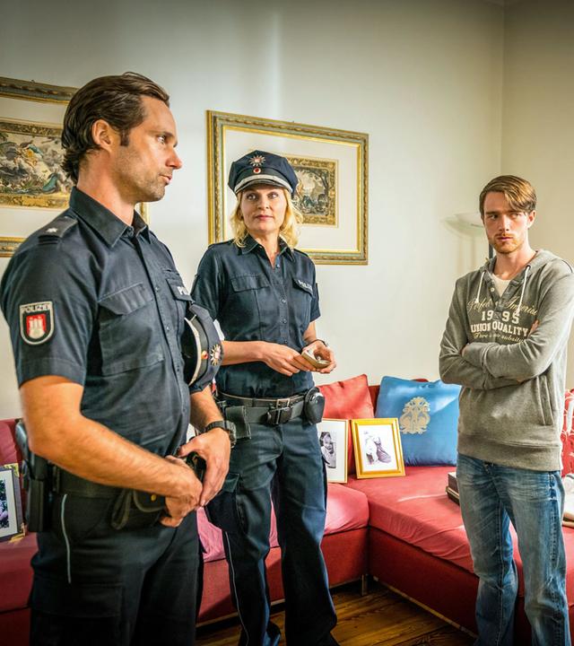 "Notruf Hafenkante - Psycho": In einem Wohnzimmer stehen der Polizeibeamte Mattes Seeler (Matthias Schloo) und seine Kollegin Melanie Hansen (Sanna Englund) Lukas Freitag (Maximilian Klas) und Karin Berger (Anne Kasprik) gegenüber.