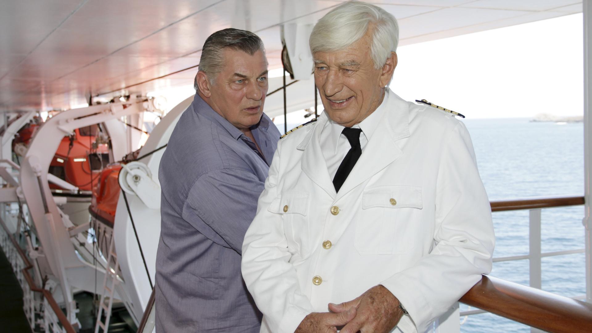 "Das Traumschiff: Puerto Rico": Paul (Heinz Hoenig) steht an der Reling der MS Amadea und blickt fragend Kapitän Paulsen (Siegfried Rauch) an. Dieser lächelt und hält die Hände gefaltet.