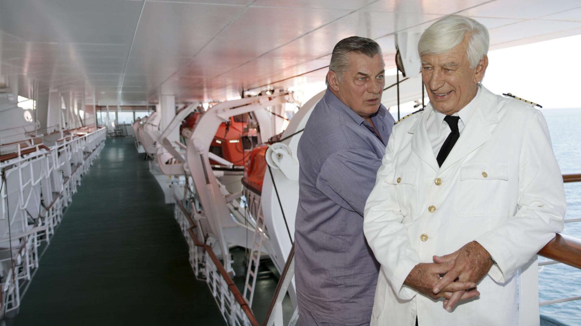 "Das Traumschiff: Puerto Rico": Paul (Heinz Hoenig) steht an der Reling der MS Amadea und blickt fragend Kapitän Paulsen (Siegfried Rauch) an. Dieser lächelt und hält die Hände gefaltet.