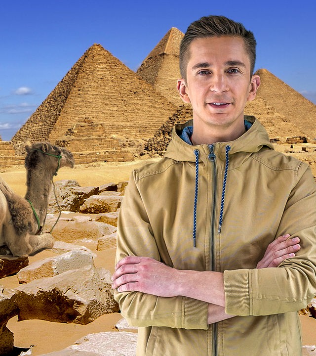 Im Vordergrund steht Moderator Eric Mayer mit verschränkten Armen. Hinter ihm ist eine Collage aus drei Pyramiden und einem liegenden Kamel zu sehen.