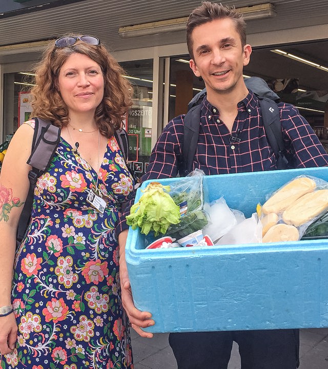 Moderator Eric (rechts) und eine Foodsaverin (links) halten eine Kühlbox gefüllt mit geretteten Lebensmitteln in die Kamera.