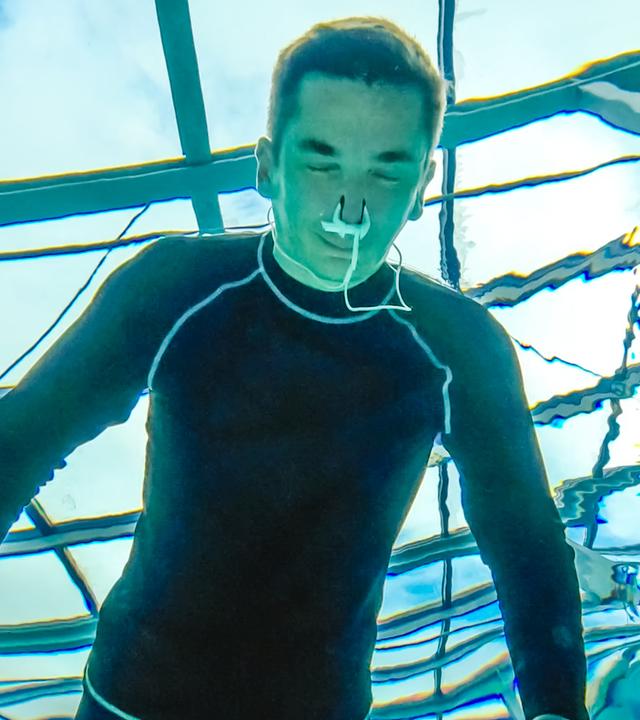 PUR+ Moderator Eric Mayer trainert in einem Neoprenanzug das Luftanhalten unter Wasser. Die Aufname zeigt ihn unter Wasser aus, wie er mit dem Gesicht unter Wasser und geschlossenen Augen sich aufs Luftanhalten konzentriert.