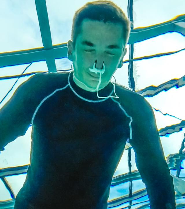 PUR+ Moderator Eric Mayer trainert in einem Neoprenanzug das Luftanhalten unter Wasser. Die Aufname zeigt ihn unter Wasser aus, wie er mit dem Gesicht unter Wasser und geschlossenen Augen sich aufs Luftanhalten konzentriert.