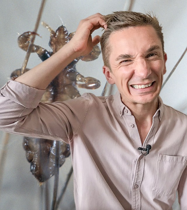 Symbolbild: PUR+ Moderator Eric Mayer steht mit dem Blick in die Kamera und kratzt sich mit der rechten Hand am Kopf. Dabei macht er ein zerknirschtes Gesicht. Im Hintergrund sieht man in Großaufnahme eine Kopflaus von unten die sich an Fäden festhält.