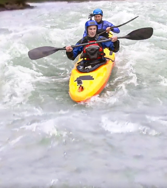 Eric Mayer sitzt in einem gelben Kajak in voller Spritzwasser-Aussrüstung und mit Helm. Hinter ihm sitzt Kajakprofi und Weltmeister Fabian Dörfler. Das Kajak fährt durch aufgewühlte Wasser. 