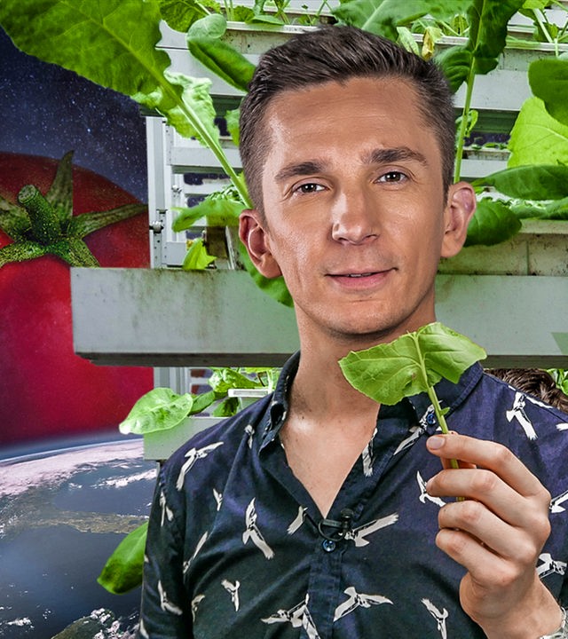 Fotomontage: Im Vordergrund rechts steht Eric Mayer. Er schaut interessiert und hält ein grünes Blatt in seiner linken Hand. Im Hintergrund ist das Weltall mit einer großen Erdkugel zu sehen. Über der Erdkugel schwebt eine riesige, rote Tomate. Hinter Eric steht ein vertikales Gemüsebeet, dass mit grünen Pflanzen bestückt ist.