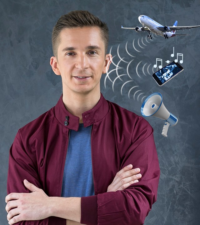 PUR+ Moderator Eric Mayer steht vor einem dunkelgrauen Hintergrund. Man sieht ihn halbnah. Er schaut uns an. Neben seinem rechten Ohr sind exemplarisch Modelle eines Flugzeugs, eines Handys und eines Megaphons zu sehen. Von ihnen gehen mit wellenlinien dargstellte Schallwellen aus in Richtung Erics rechtes Ohr.