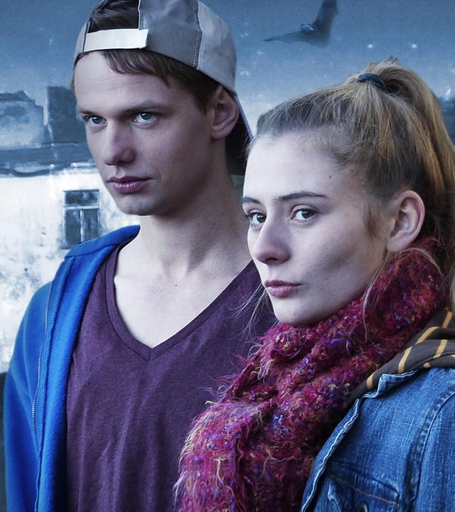 Jugendliches Mädchen und jugendlicher Junge (farbig) stehen vor einem Haus (in schwarz-weiß). Das Haus ist zum Teil schon eingefallen. Beide schauen eingeschüchtert und ängstlich aus.