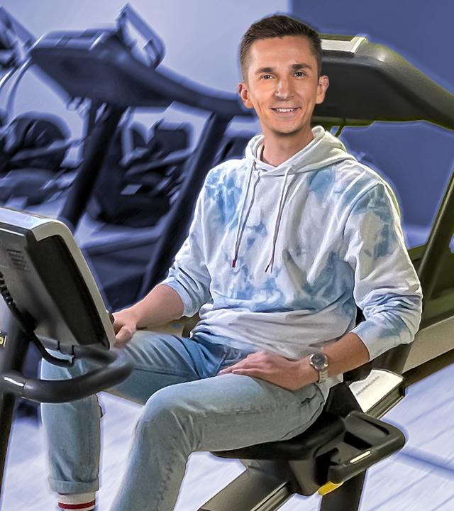 Moderator Eric Mayer sitzt auf einem Ergometer umgeben von vielen weiteren Ergometern.