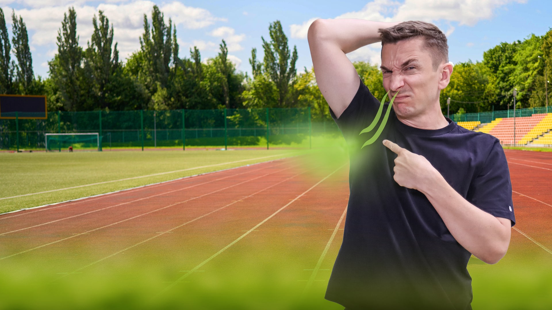 Moderator Eric Mayer hebt den linken Arm und riecht mit der Nase an seiner linken Achsel. Dabei verzieht er das Gesicht und zeigt mit dem rechten Zeigefinger auf die Achsel. Er trägt ein schwarzes T-Shirt. Im Hintergrund ist ein Sportplatz zu sehen.