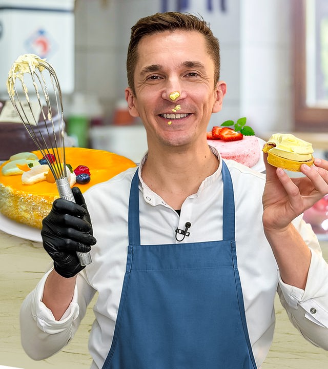 Eric Mayer steht in einer Küche und schaut freudig in die Kamera. Er trägt ein weißes Hemd und darüber eine blaue Schürze. In der rechten Hand hält er einen mit Creme verschmierten Schneebesen. In der linken Hand hält er ein Mini-Törtchen. Auf seiner Nase und rund um den Mund sind Kleckse aus Tortencreme. Um ihn herum stehen auf einer Küchenarbeitsplatte drei verschiedene Torten platziert.