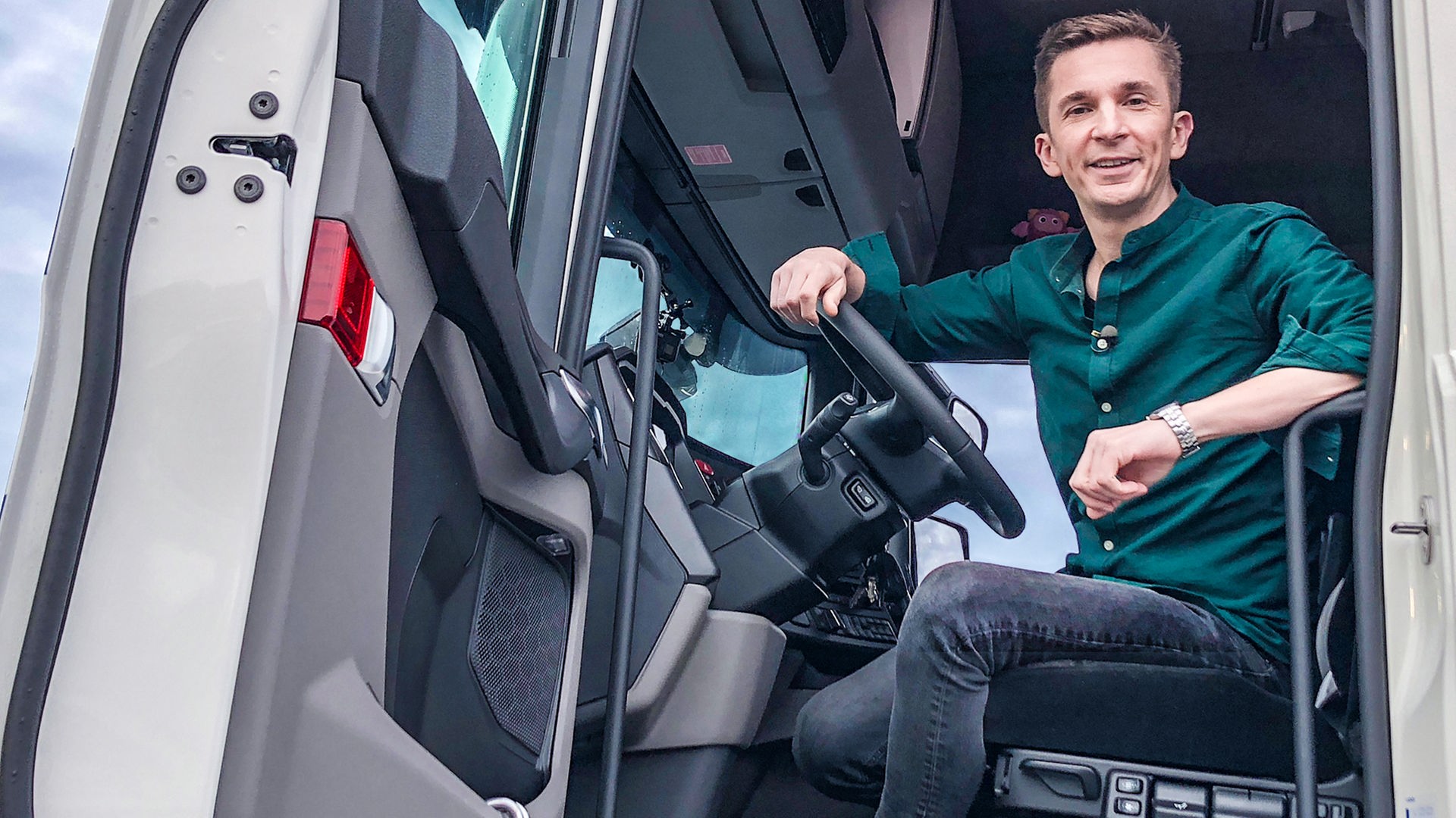 Moderator Eric Mayer sitzt im Fahrerhaus eines weiß-blauen LKW. Die Tür steht offen.