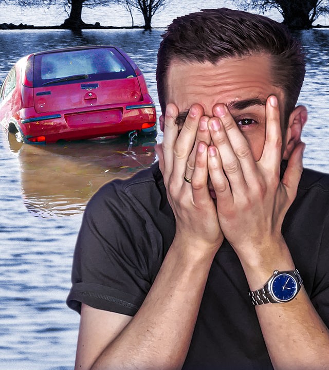 Moderator Eric Mayer ist rechts im Bild. Er hält sich die Hände vors Gesicht und schaut zwischen den Fingern angsterfüllt hindurch. Im Hintergrund sieht man, wie ein rotes Auto beginnt, im Wasser eines Flusses zu versinken.
