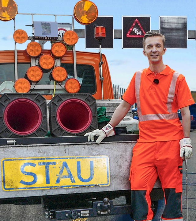 PUR+ Moderator Eric Mayer steht in orangefarbener Arbeitskleidung am Heck eines Baustellenfahrzeugs. Dieses hat auf der Ladefläche ein großes Warnkreuz mit Signallampen und ein Schild mit dem Schriftzug "Stau".