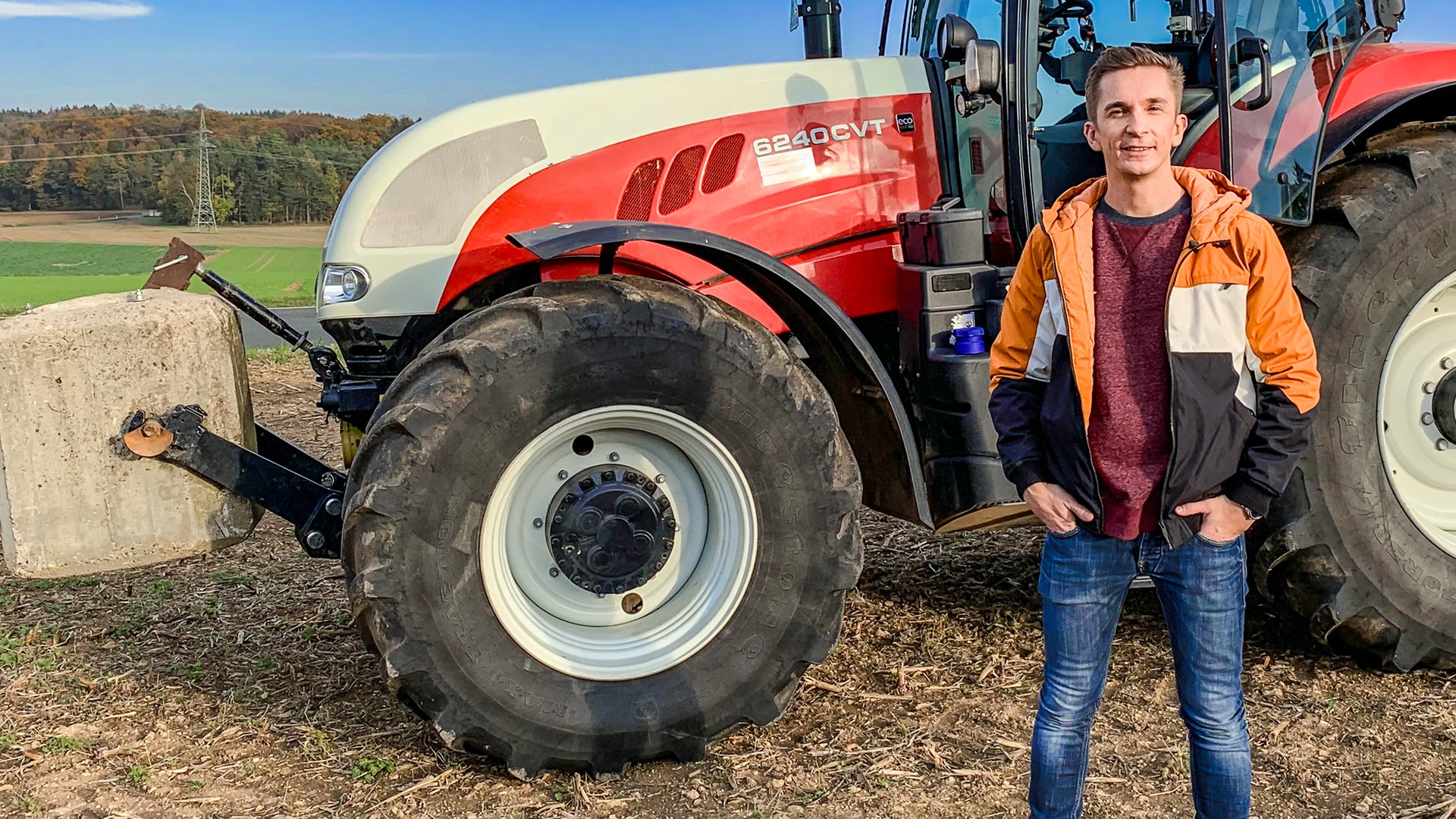 Moderator Eric Mayer steht seitlich neben einem großen Traktor.