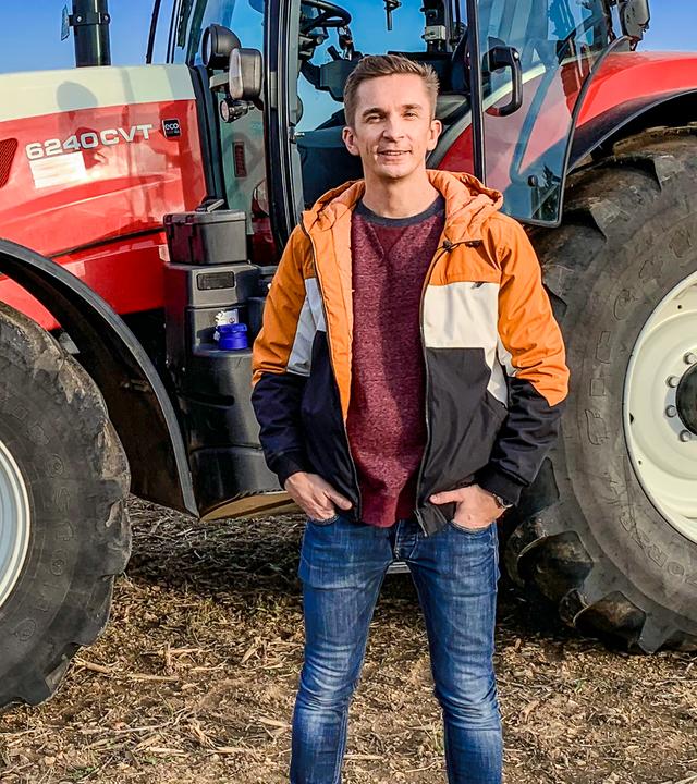 Moderator Eric Mayer steht seitlich neben einem großen Traktor.