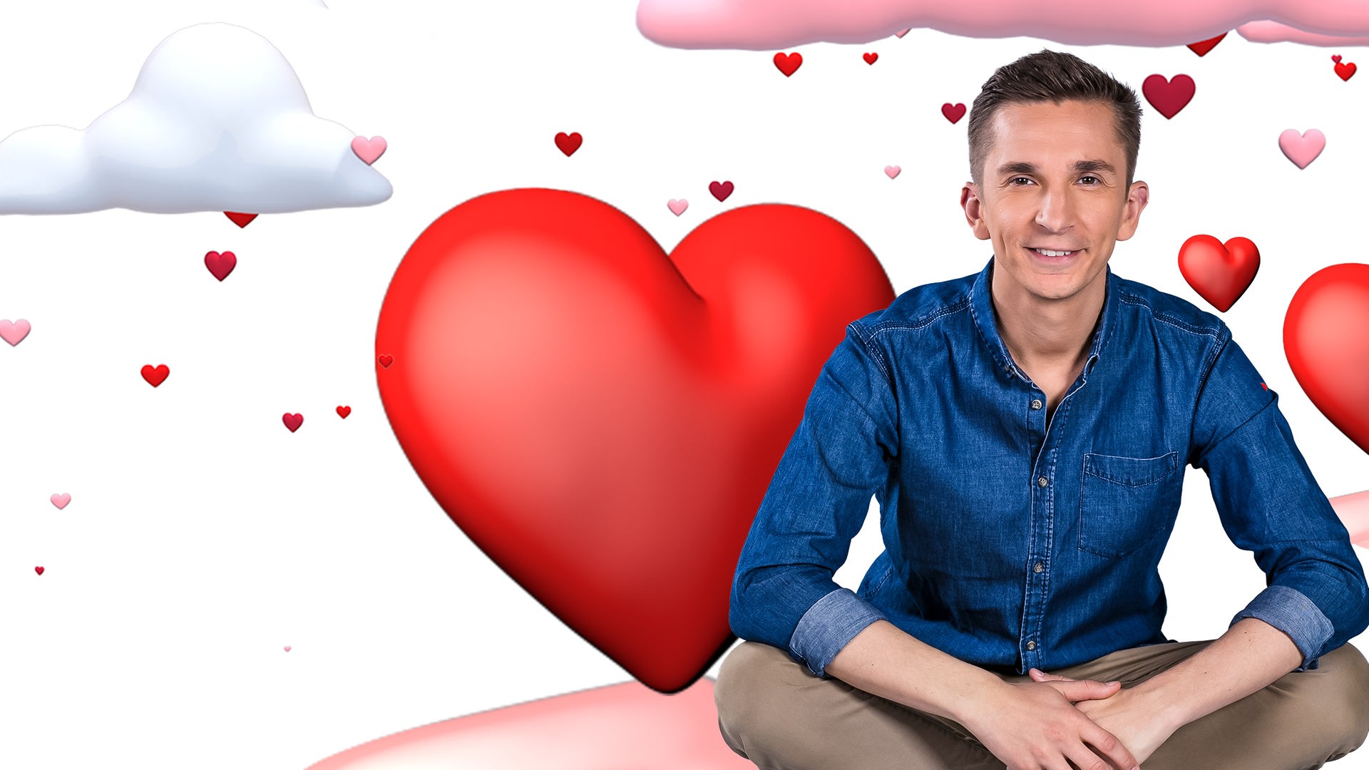 Moderator Eric Mayer sitzt im Schneidersitz und lächelt in die Kamera. Er sitzt vor einem weißen Hintergrund der gefüllt ist mit roten und rosa Herzen in verschiedenen Größen und mit weißen und rosafarbenen Wolken.