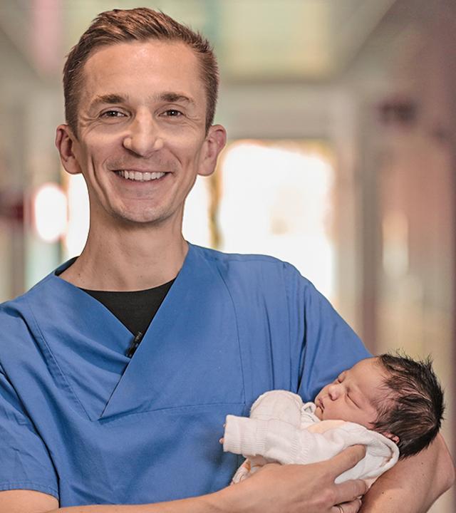 Moderator Eric hält im Krankenhaus ein Baby auf dem Arm.