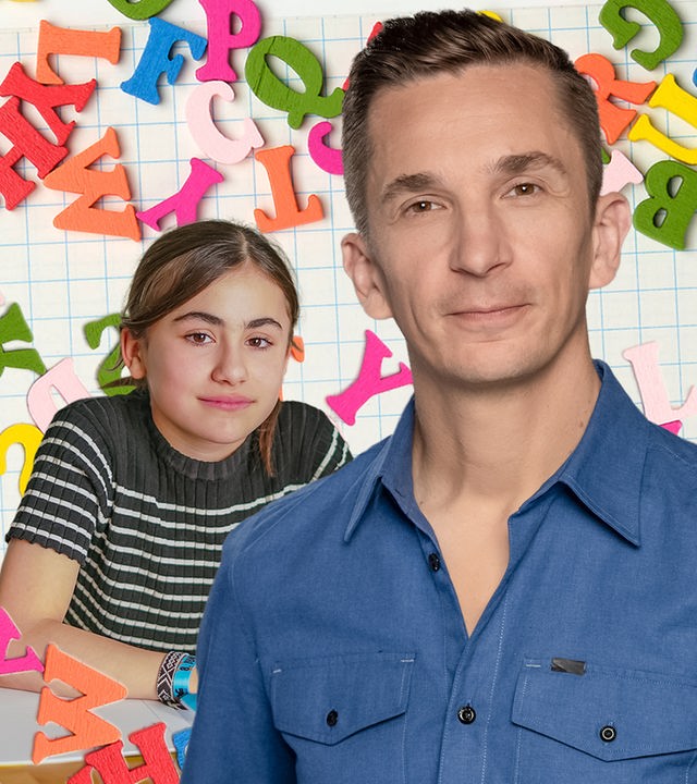 Eric schaut in die Kamera, hinter ihm bunte Buchstaben und Zahlen auf einer Tafel und ein Mädchen mit einem Schulheft.