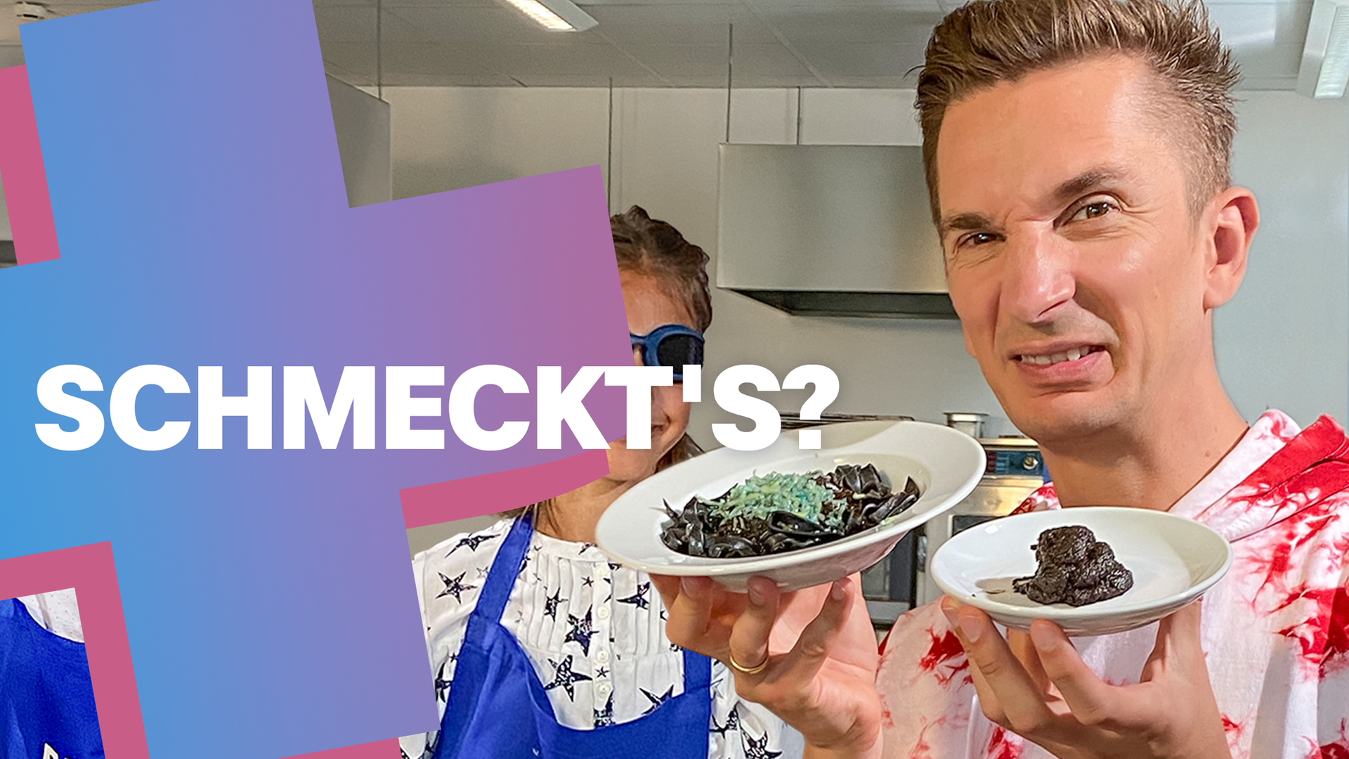 Eric hält mit angeekeltem Blick einen Teller in die Kamera, auf dem etwas Braunes, ekelig aussehendes liegt. Hinter ihm sieht man einen Jungen mit verbundenen Augen.