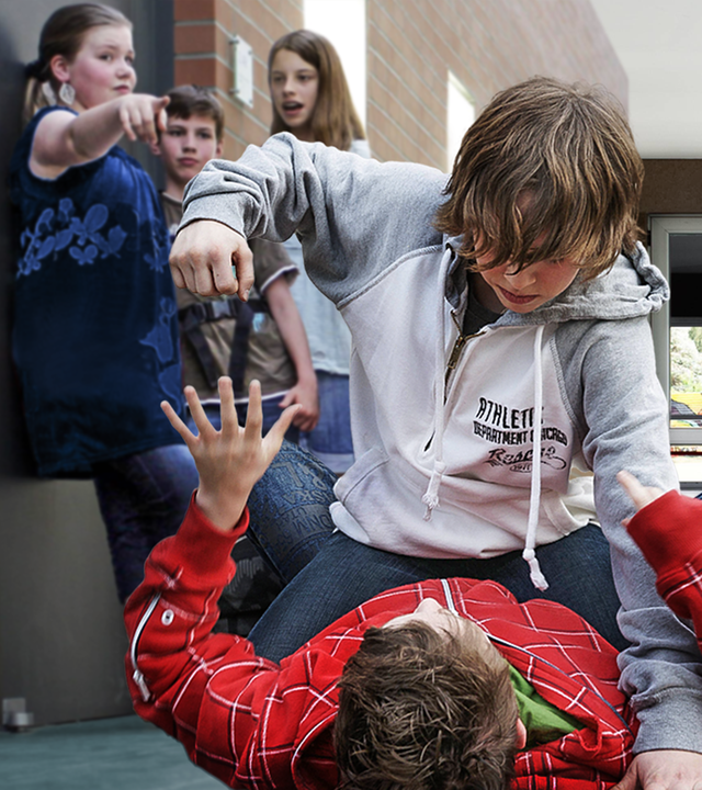 In einem Schulflur: Auf dem Boden liegt ein Junge. Ein anderer Junge kniet über ihm und scheint ihn schlagen zu wollen. Links an der Wand im Flur stehen zwei Schülerinnen und ein Schüler. Sie beobachten den Streit. Ein Mädchen zeigt mit der rechten Hand in Richtung der streintenden Jungen am Boden.