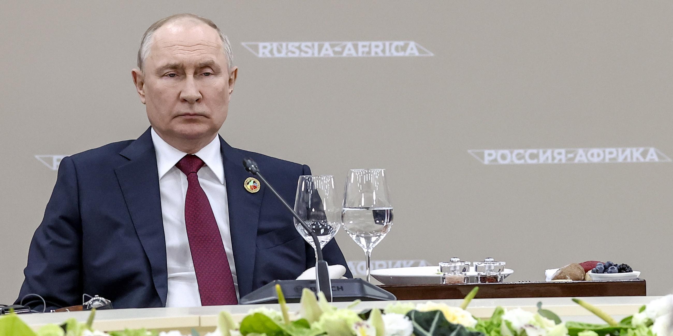 Zu sehen ist Präsident Putin an einem Konferenztisch mit Blumen im Vordergrund.