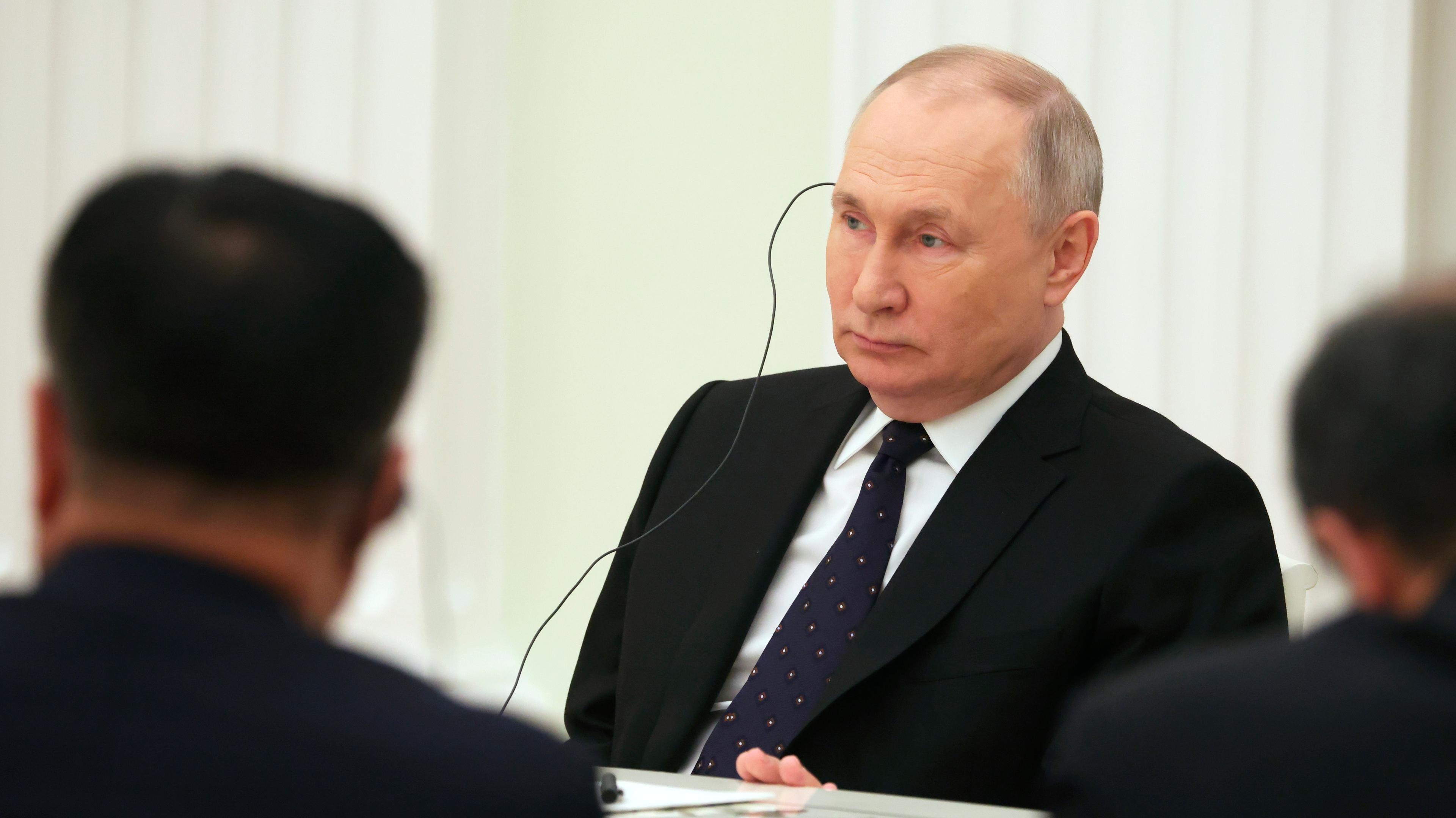 Der russische Präsident sitzt an einem Tisch und hört über einen Kopfhörer einer Übersetzung zu