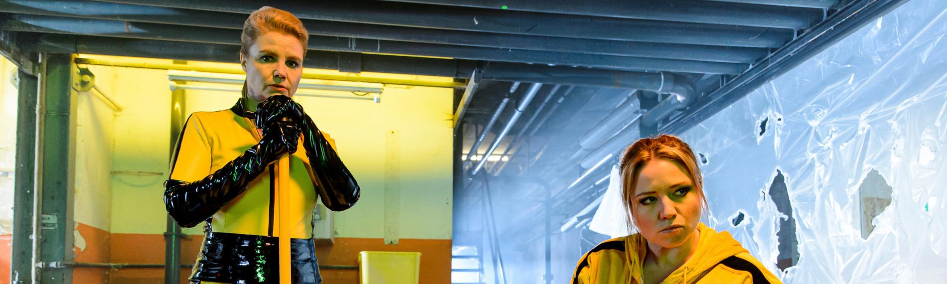 Caro Frier und Anette Frier stehen in gelben Schutzanzügen in einem Labor.