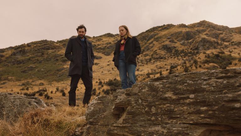 "Queenstown Murders – Zum Sterben schön - Am Abgrund": Anais (Chelsie Preston Crayford) und Simon (Matt Whelan) stehen nebeneinander am Rand eines Canyons. Sie blicken nach unten.