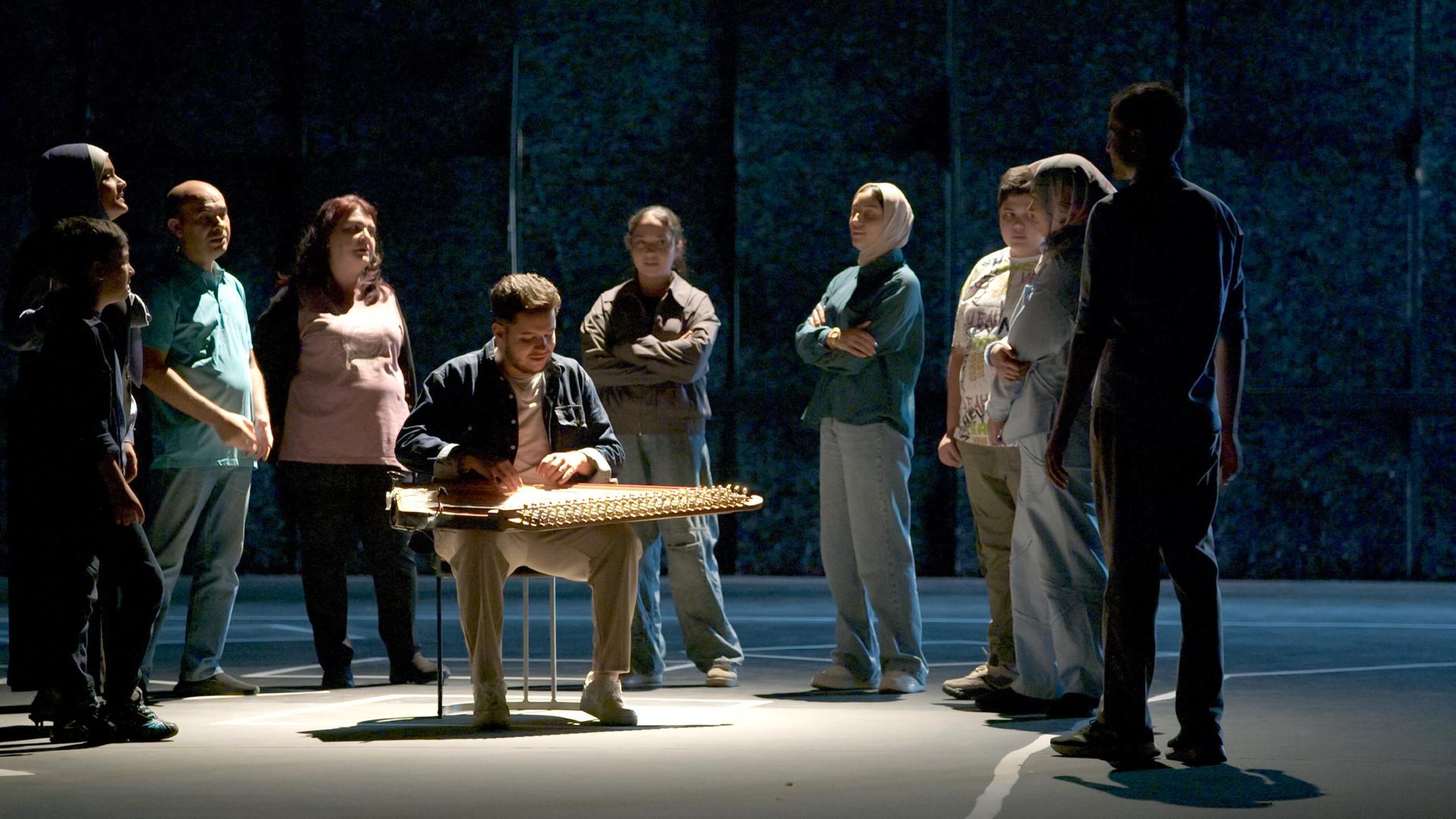 Auf einer Bühne steht eine Gruppe Menschen um einen Musiker, der ein orientalisches Zupfinstrument spielt.