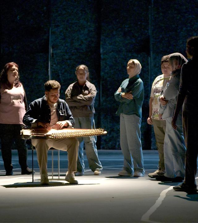 Auf einer Bühne steht eine Gruppe Menschen um einen Musiker, der ein orientalisches Zupfinstrument spielt.