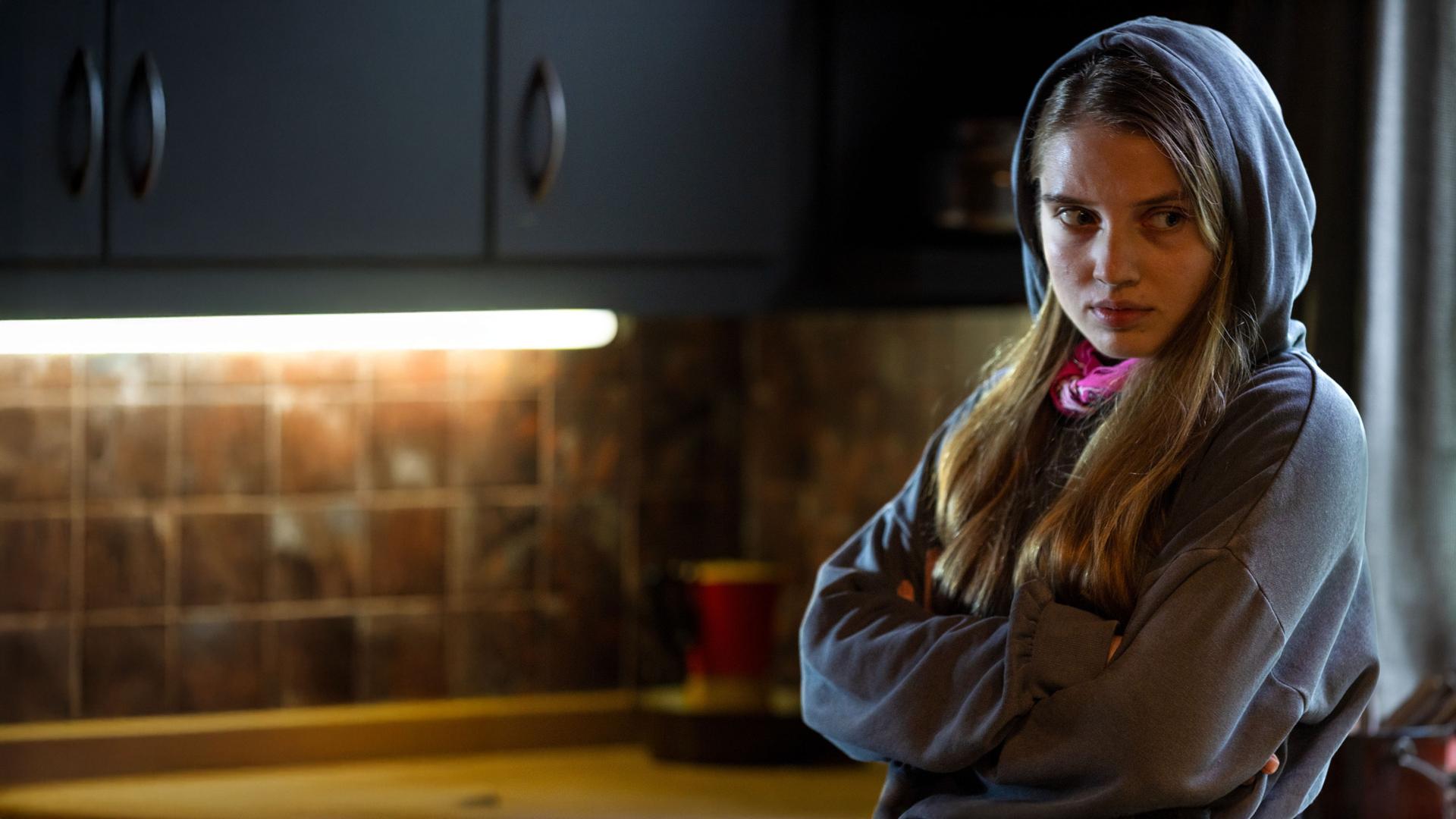 "The Kollective - Quid pro quo": Anna (Veronika Mox) steht mit verschränkten Armen in einem Raum mit dem Rücken zu einem Fenster. Sie trägt einen Hoodie und wirkt verärgert.