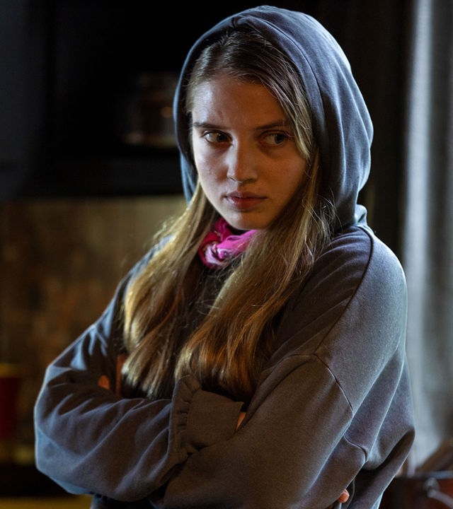 "The Kollective - Quid pro quo": Anna (Veronika Mox) steht mit verschränkten Armen in einem Raum mit dem Rücken zu einem Fenster. Sie trägt einen Hoodie und wirkt verärgert.