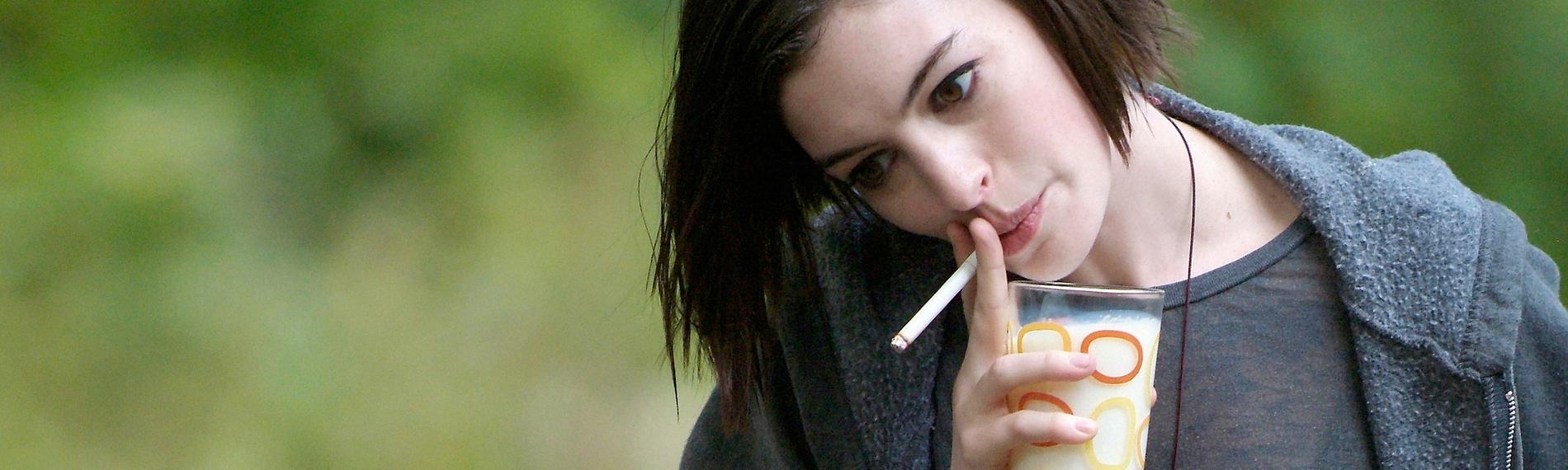 Kym (Anne Hathaway) hält einen Teller mit belegten Broten in der einen Hand und steckt sich mit der anderen eine Zigarette in den Mund.