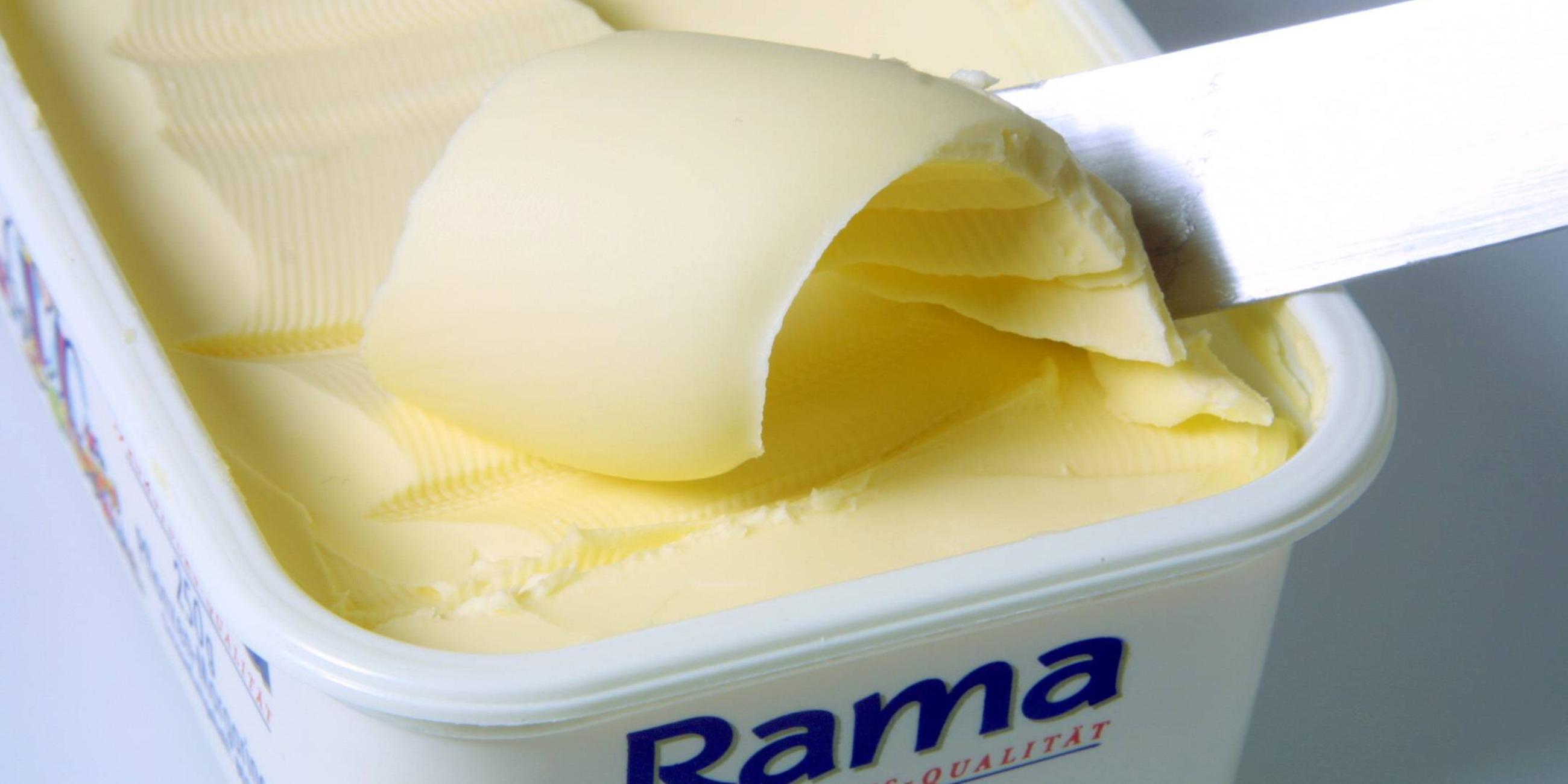 Margarine wird mit dem Messer aus einem Becher gestrichen