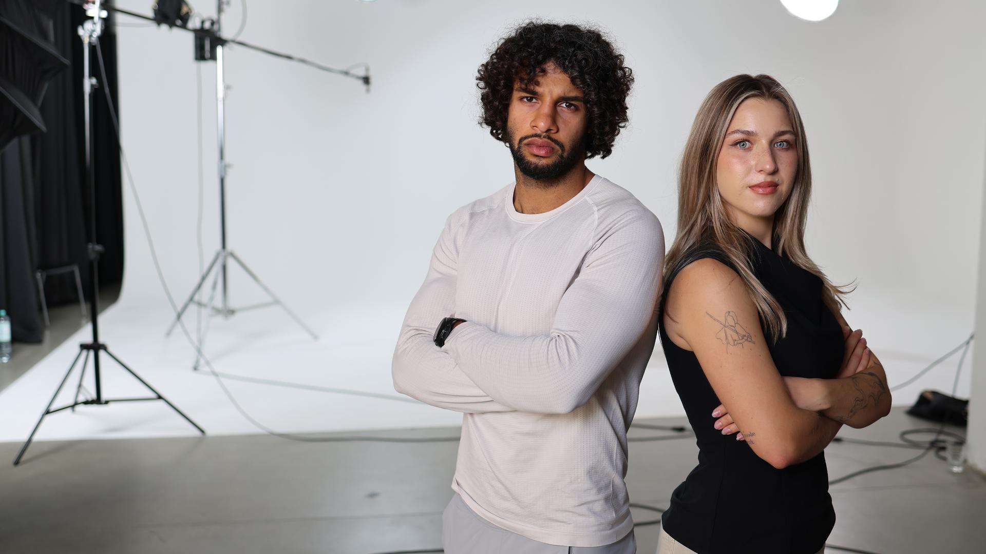 Fitness-Creator Rami Al-Azzawi (links) und Psychologiestudentin Julia Barabasch (rechts) stehen Rücken an Rücken und mit verschränkten Armen rechts im Bild.