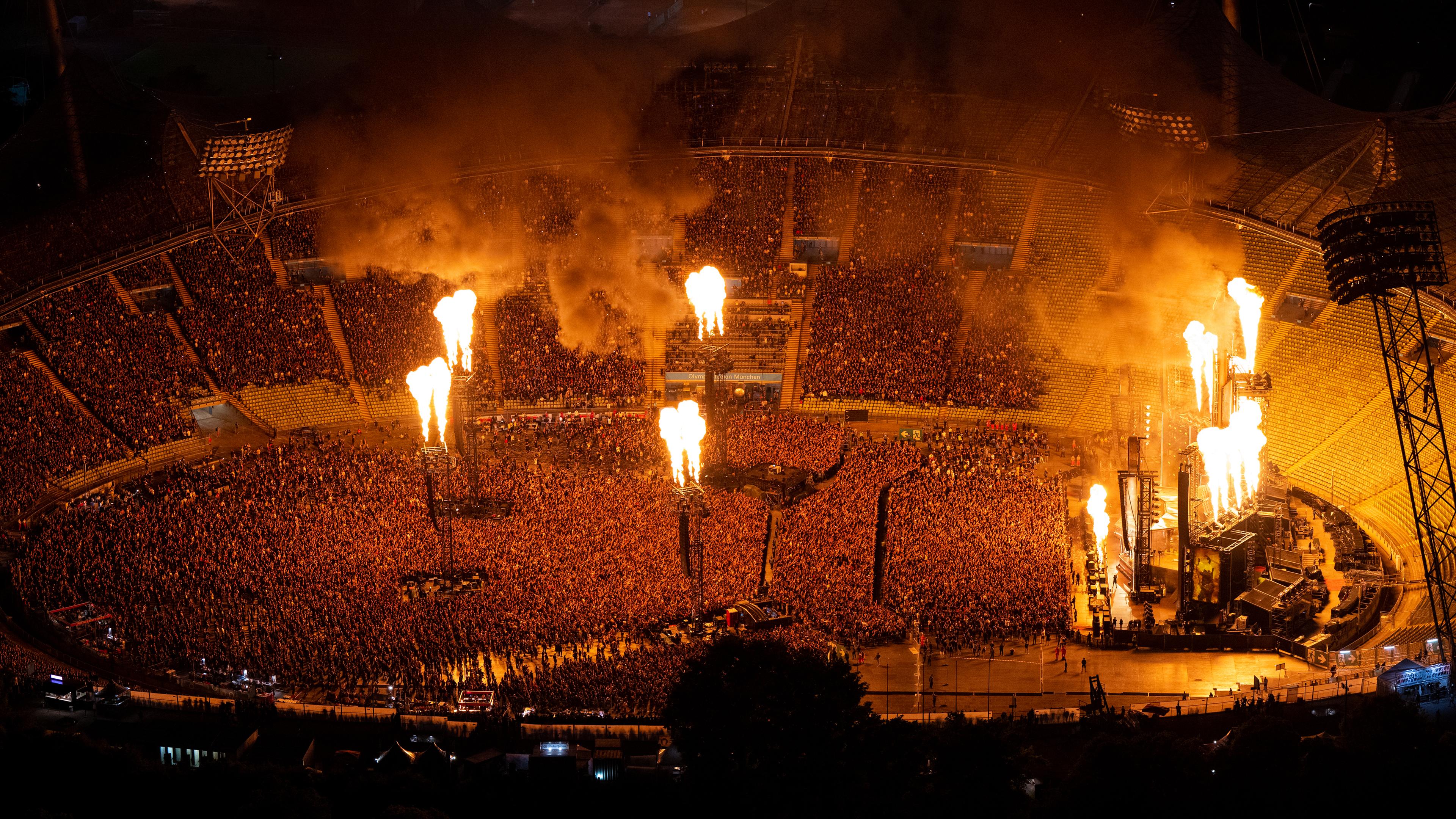 Tausenden Menschen sind von oben vor der Bühne im Olympiastation zu sehen, erleuchtet durch Flammenwerfer im Stadion.