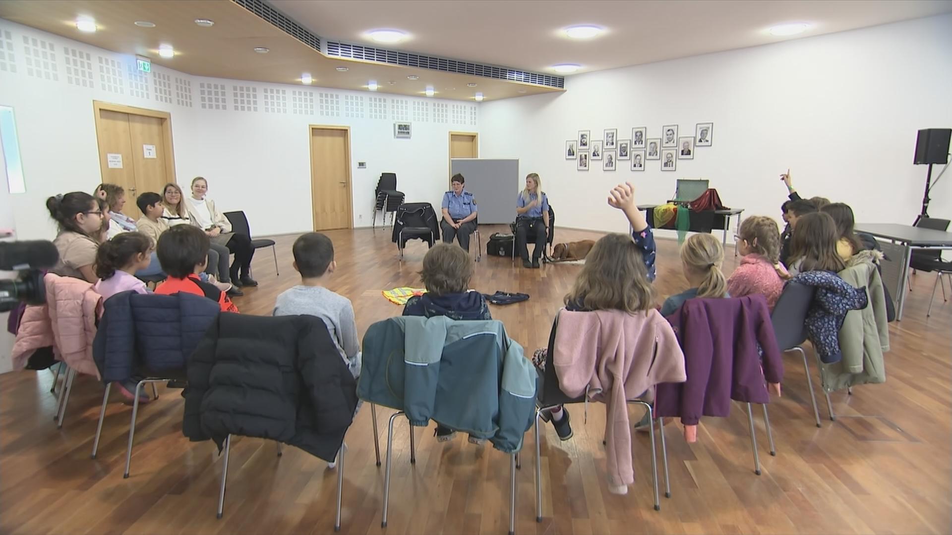 Auf dem Bild sieht man zwei Polizistinnen, die Kindern etwas vorlesen.