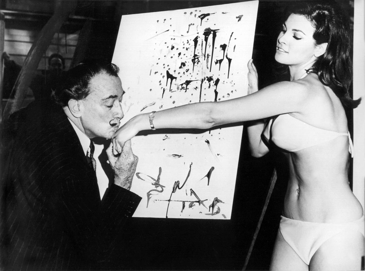 Der spanische Maler Salvador Dali küsst Raquel Welch die Hand, während sie dem Künstler im Schaufenster eines New Yorker Geschäftes Modell steht.