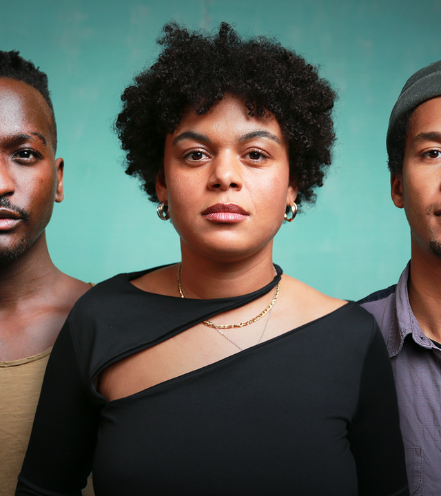 Zwei Männer und eine Frau stehen nebeneinander und blicken in die Kamera. Alle drei sind schwarz.