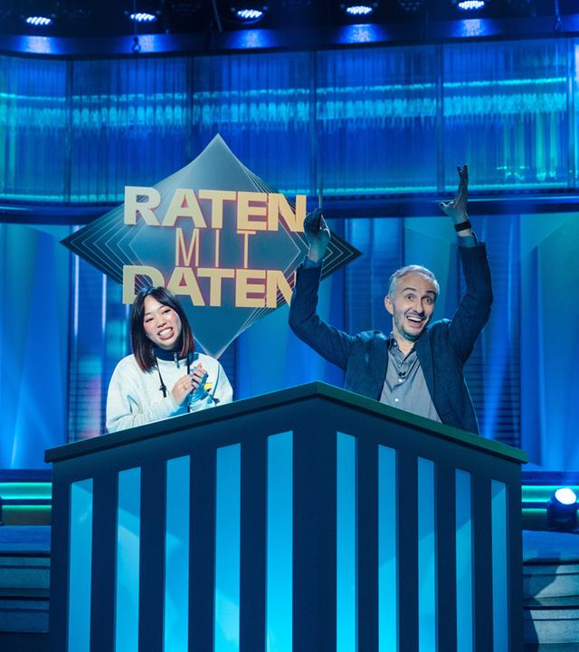 In der Show: Jan Böhmermann und Kandidatin Lilien sitzen auf der Bühne. Jan Böhmermann jubelt, die Kandidatin wird überrascht.