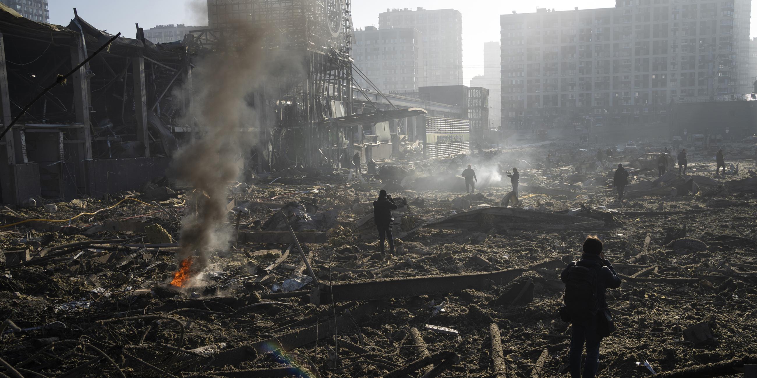 Archiv: Menschen gehen durch die rauchenden Trümmer inmitten der Zerstörung, die nach dem Beschuss eines Einkaufszentrums in Kiew entstanden ist. 
