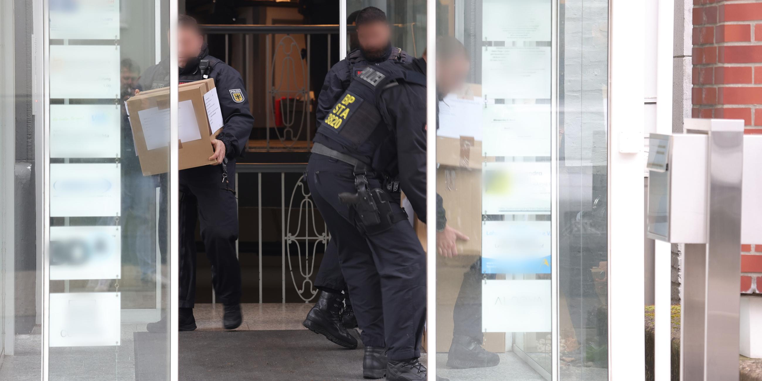 Polizeibeamte tragen in Kartons sichergestelltes Material aus einem Gebäude. 