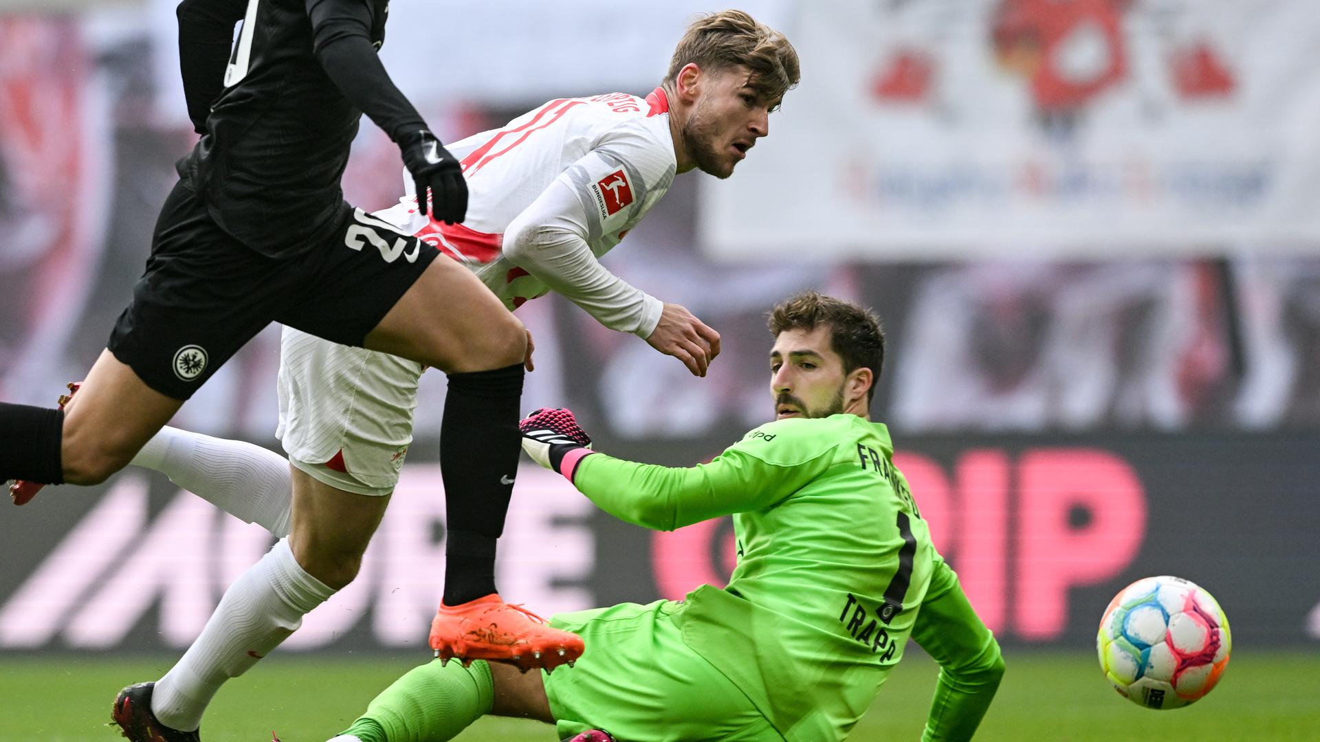 Der Leipziger Timo Werner erzielt beim Bundesliga-Fußballspiel zwischen RB Leipzig und Eintracht Frankfurt neben Frankfurts Makoto Hasebe (L) und Frankfurts Torhüter Kevin Trapp den Führungstreffer, 25.02.2023, in Leipzig
