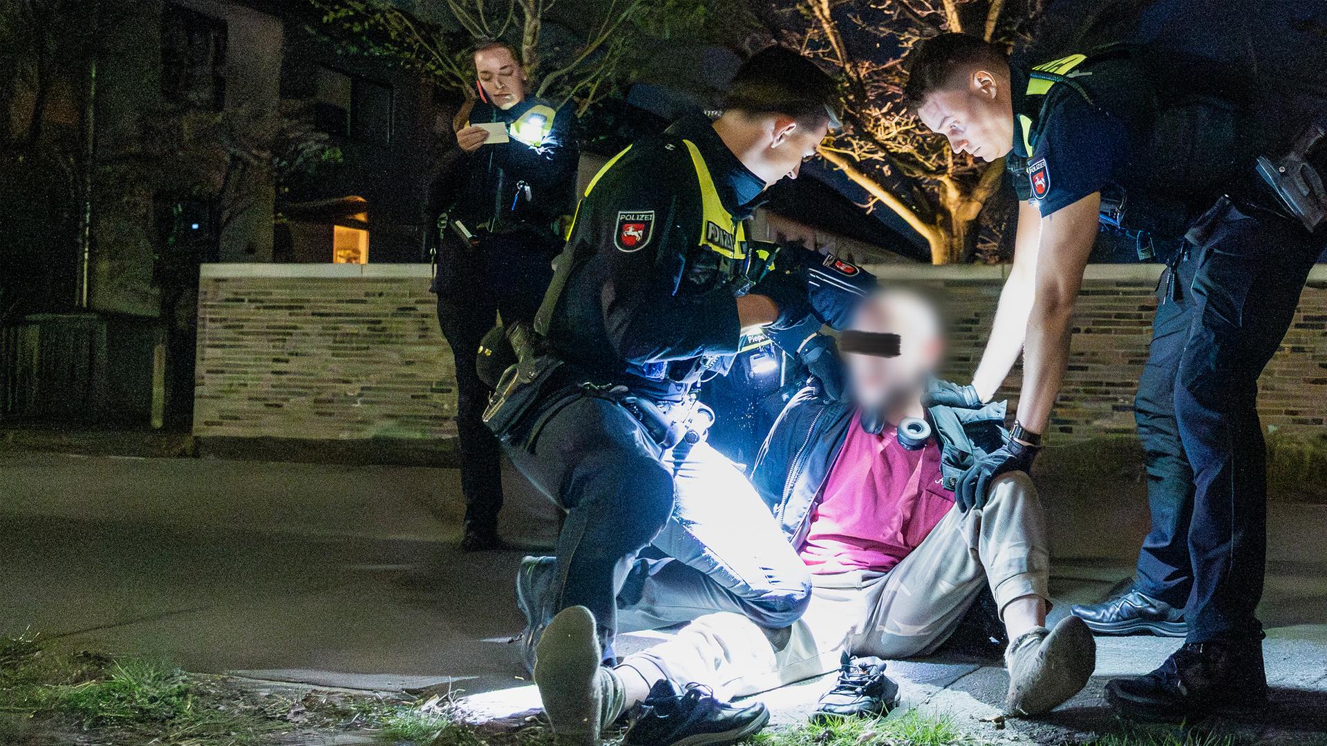 Zwei Polizisten halten auf einer Wiese einen Mann am Boden.