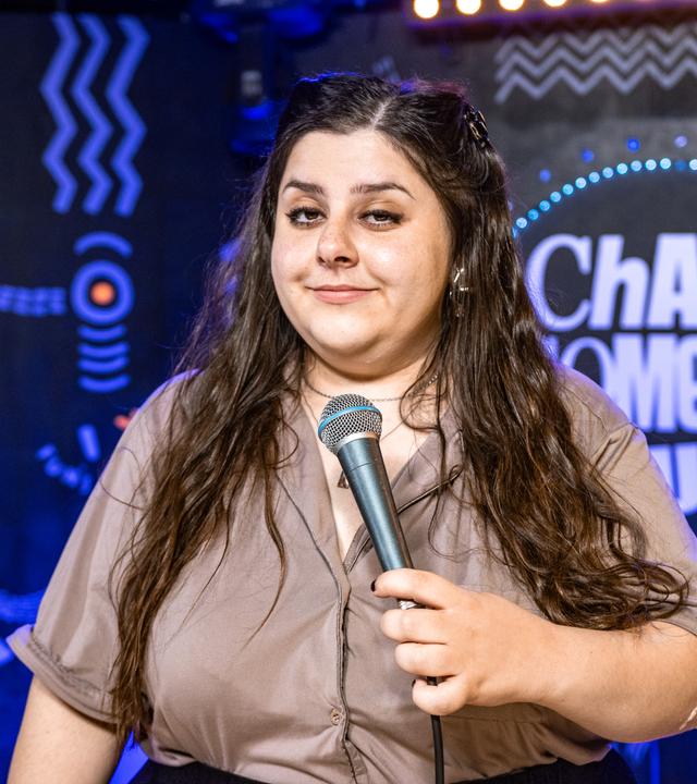 Rebecca Pap ist in der Mitte des Bildes zu sehen. In ihrer linken Hand hält sie ein Mikrofon.