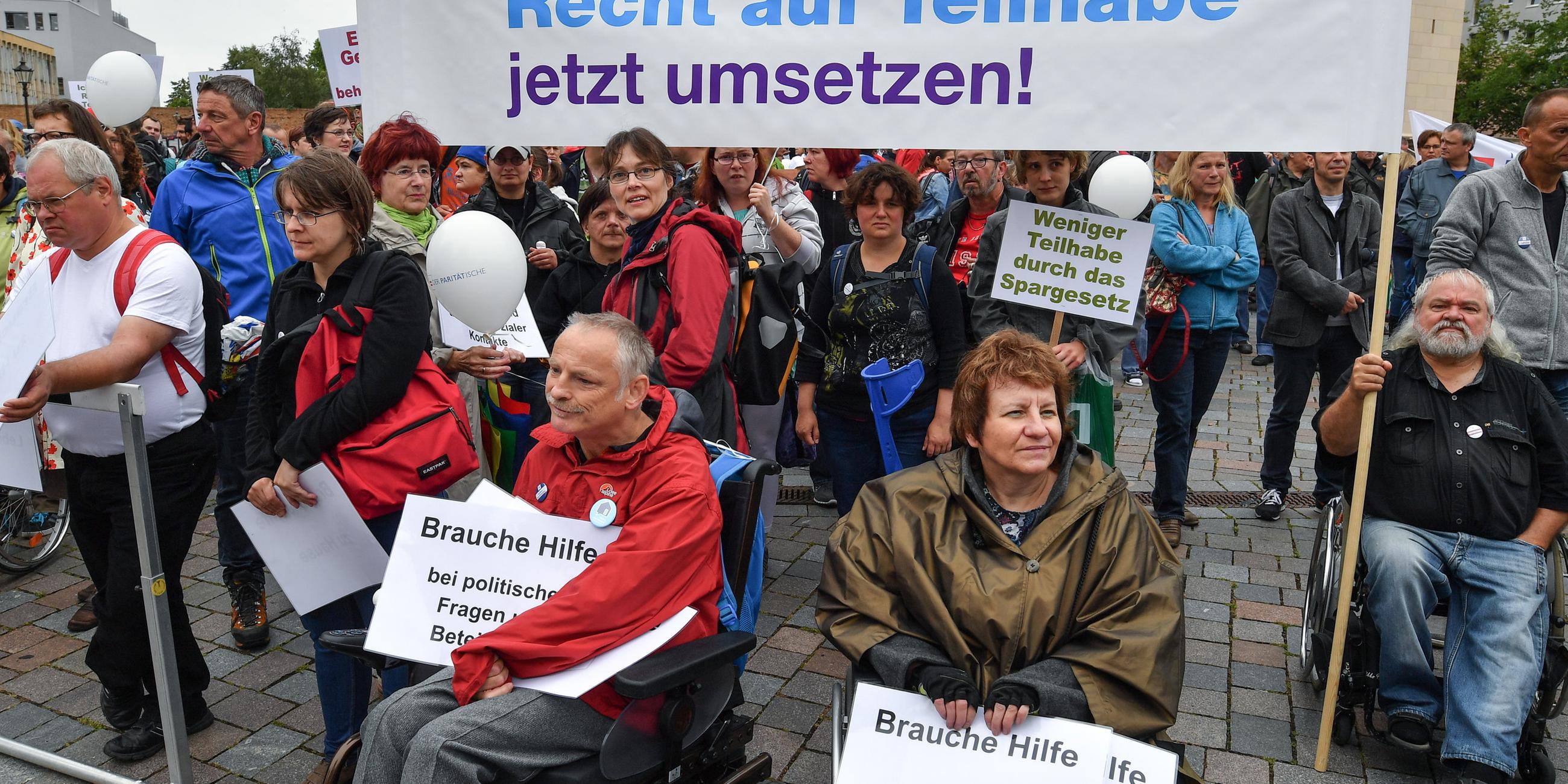 Behinderte und nichtbehinderte Menschen nehmen an einer Protestaktion teil. In der Menge ein Trant mit dem Schriftzug "Recht auf Teilhabe jetzt umsetzen".